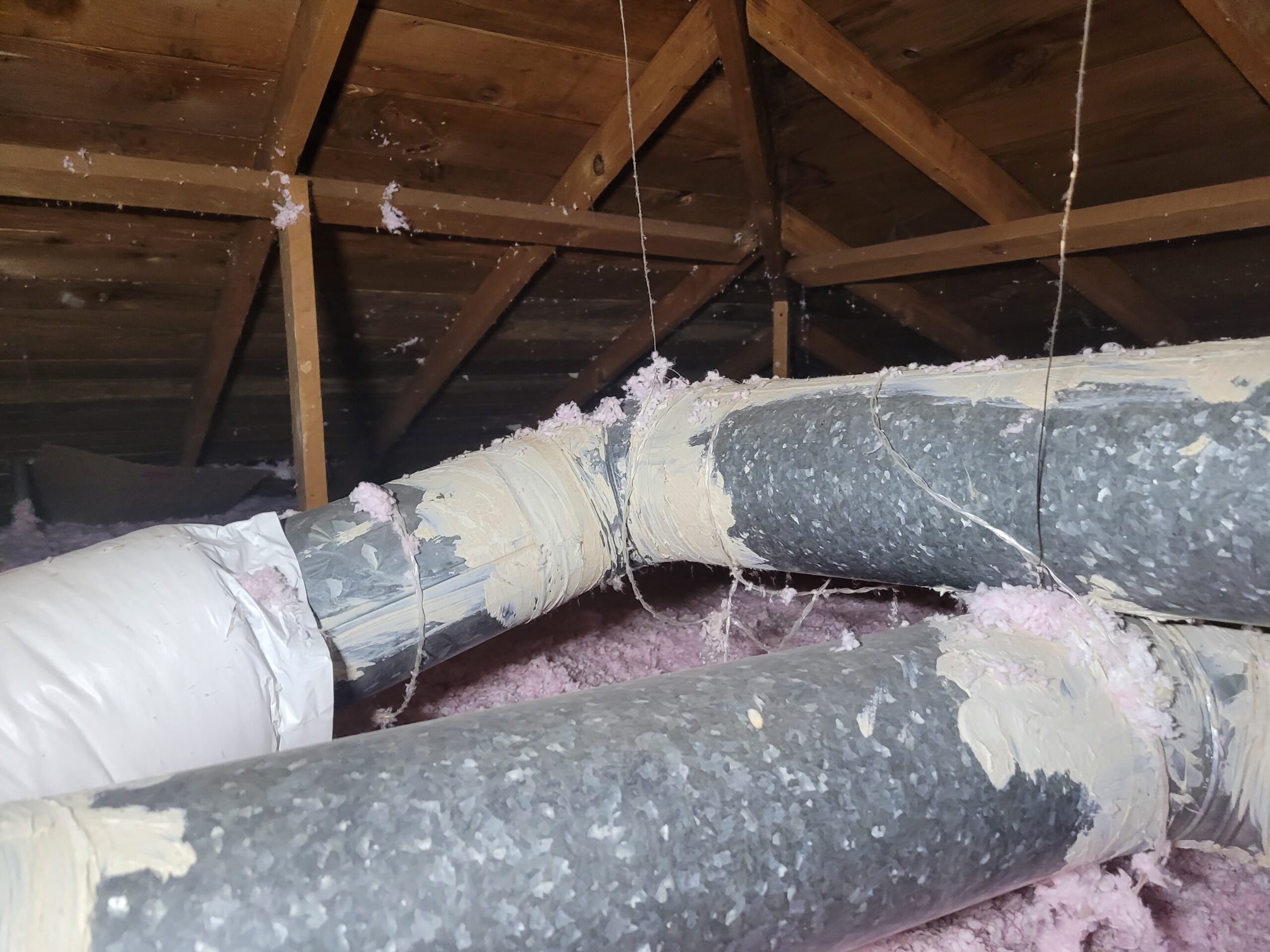 Insulated flexible ductwork in an attic with mastic-sealed joints and blown-in fiberglass insulation
