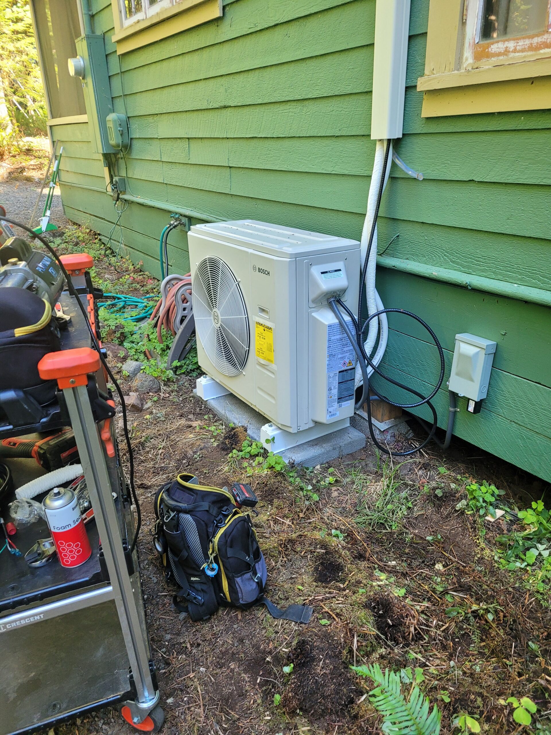 Bosch mini-split heat pump outdoor unit newly installed on a concrete pad with installation tools nearby