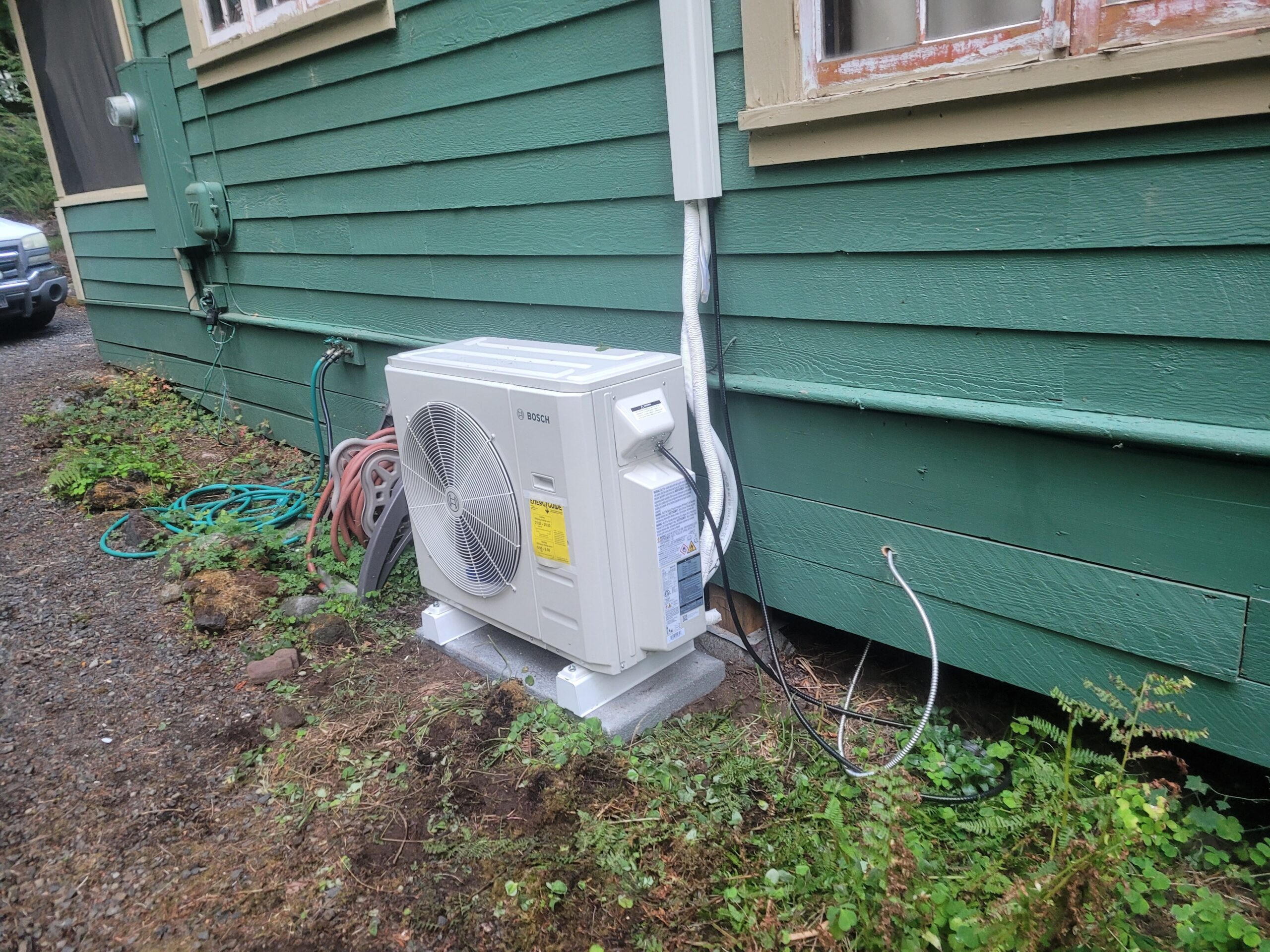 Bosch mini-split heat pump condenser installed on a concrete pad with refrigerant lines routed into the home