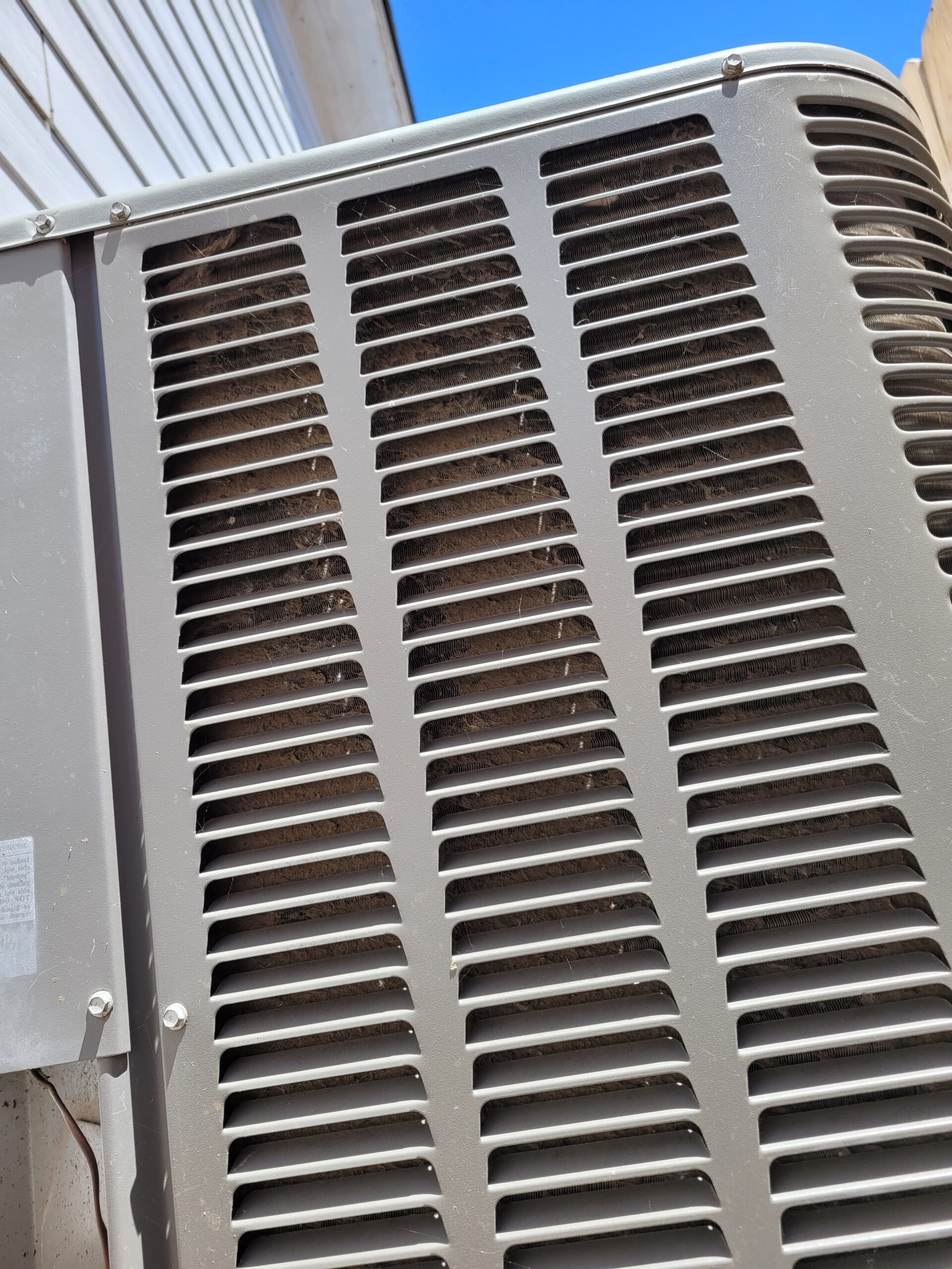 Outdoor AC condenser unit with visibly dirty and clogged condenser coils seen through the grille