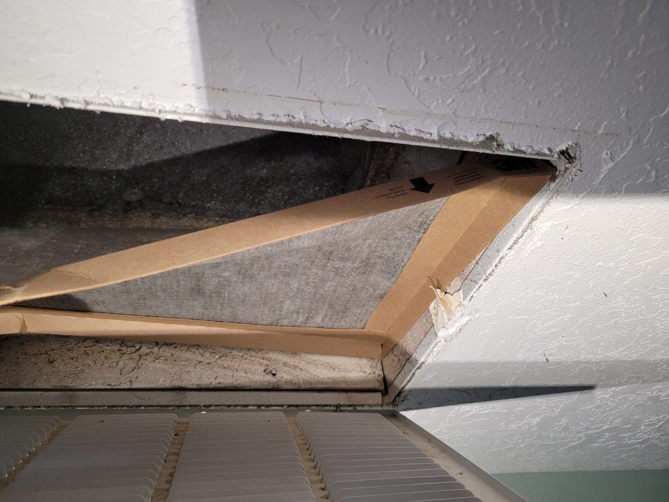 Dirty air filter being pulled from a ceiling HVAC return vent showing heavy dust accumulation