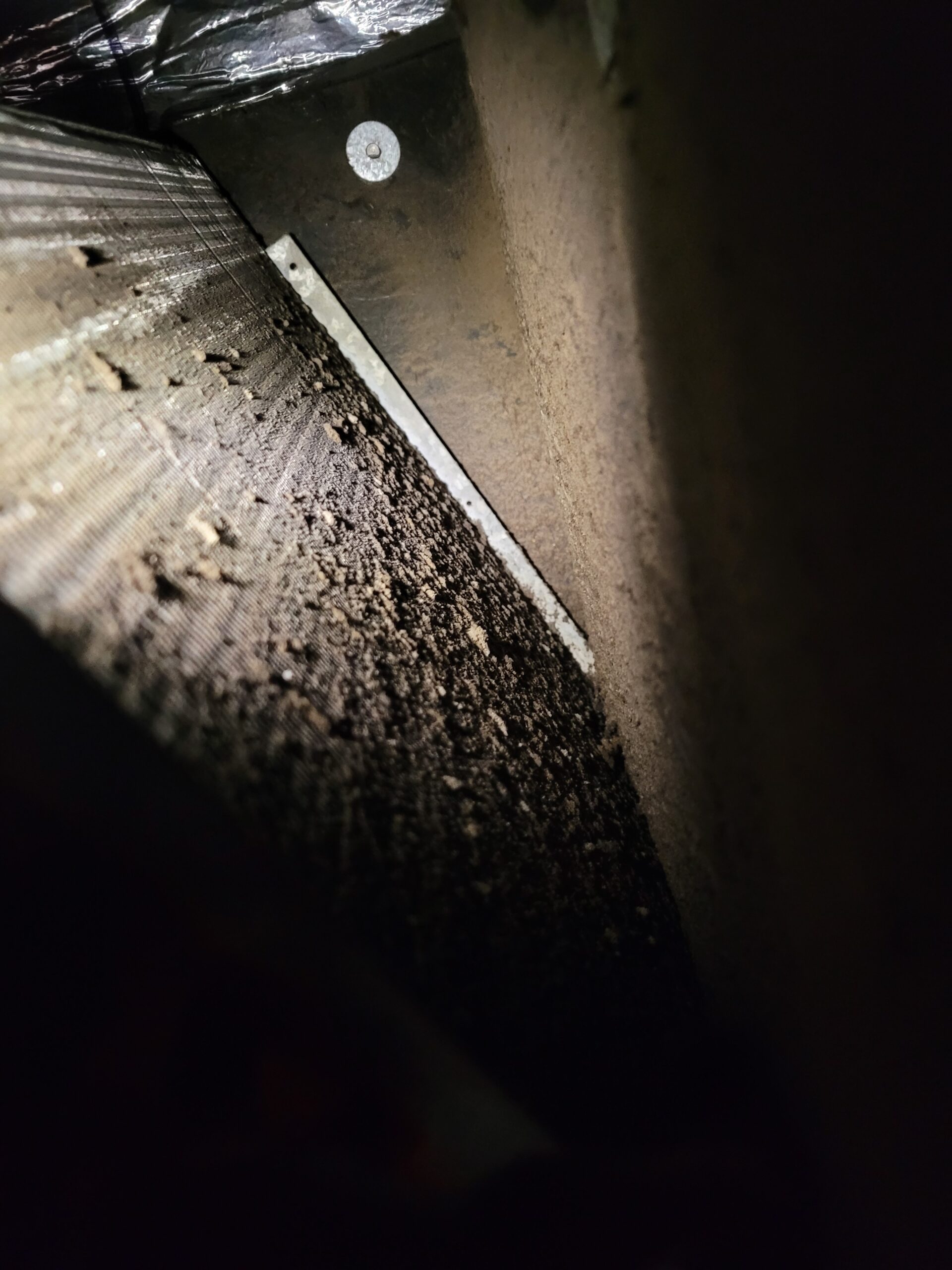 Heavy dust and debris buildup inside an HVAC air duct near a metal seam