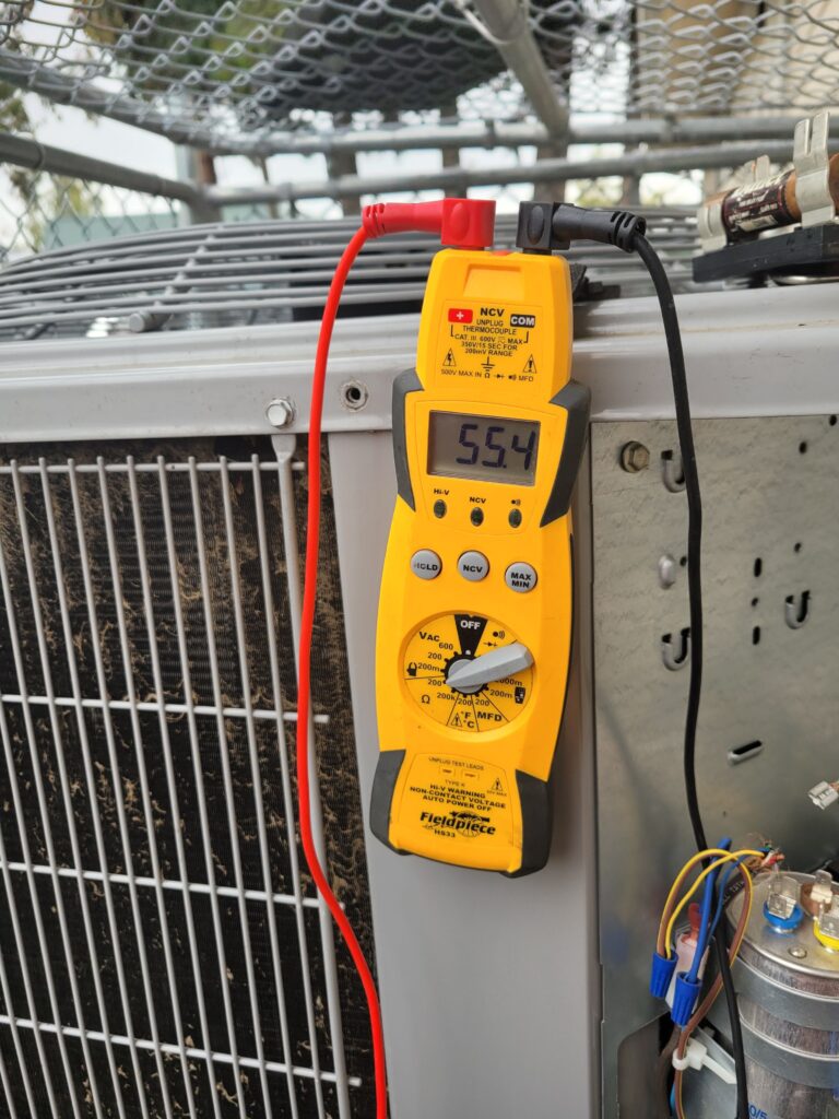 Fieldpiece HS33 multimeter displaying 55.4 MFD while testing a capacitor on an outdoor HVAC condenser unit