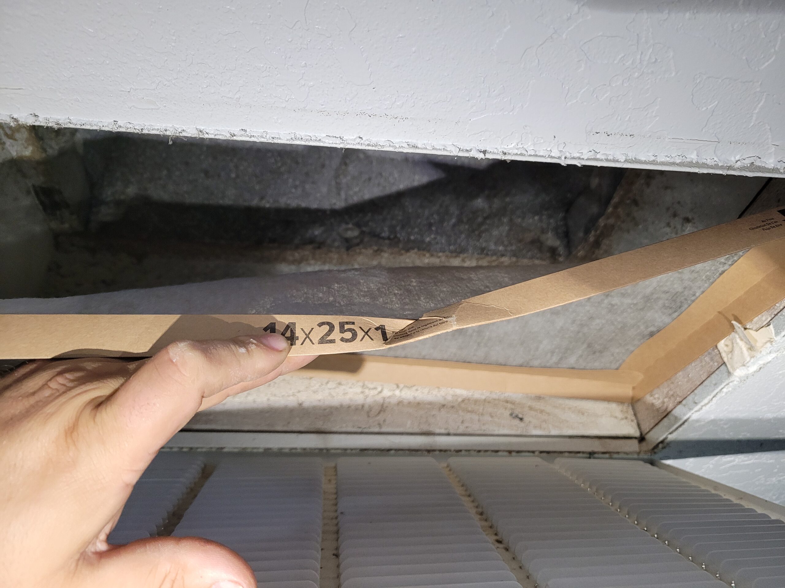 Hand pointing to the size label reading 14x25x1 on an HVAC air filter pulled from a return air vent