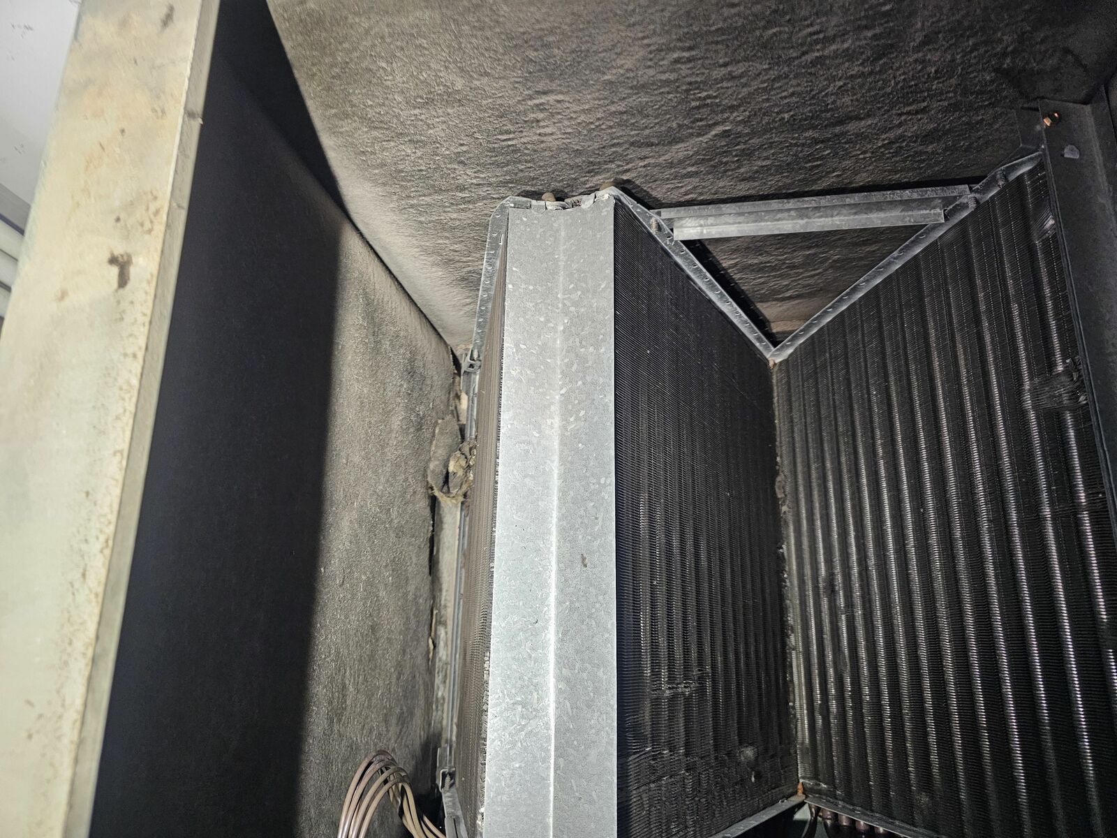 Interior of an HVAC air handler showing V-shaped evaporator coils with visible dust buildup