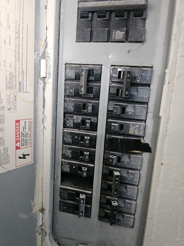 Open residential electrical breaker panel showing multiple circuit breakers of various amperages (20, 30, 40 amp) with a danger warning label on the inside of the door