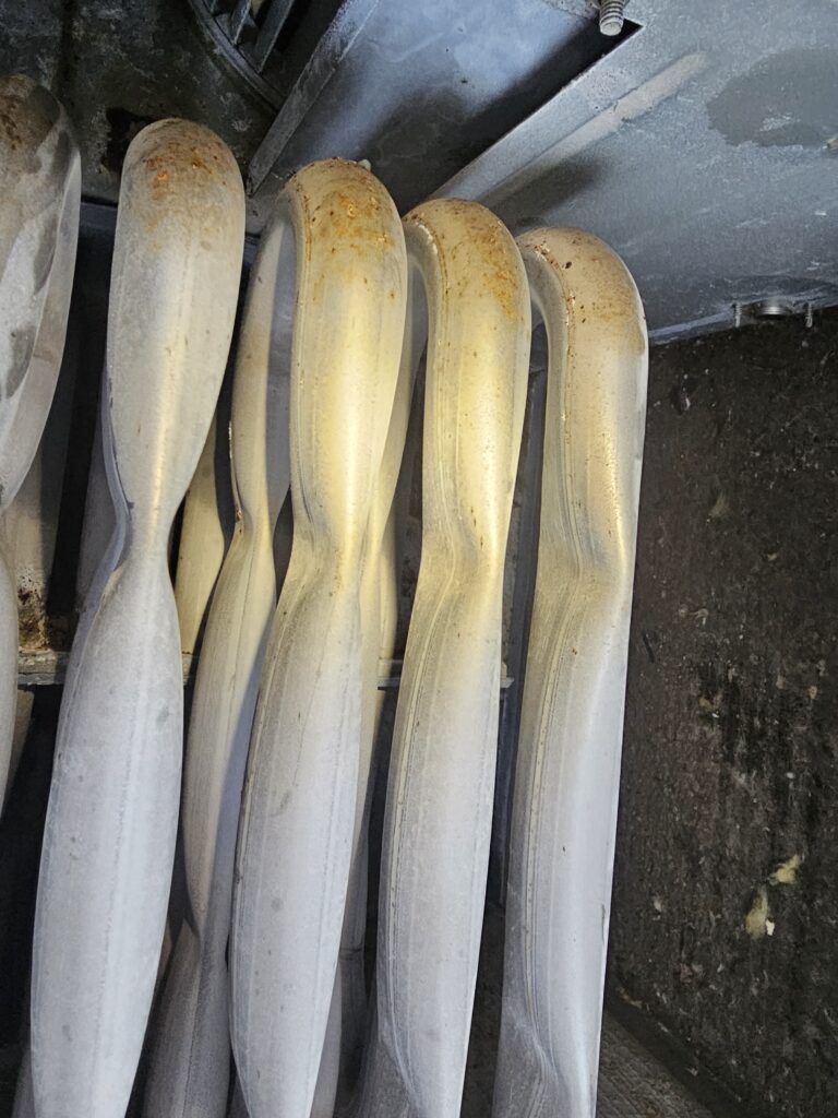 Close-up of furnace heat exchanger tubes with rust spots on the upper bends inside a dusty, insulated cabinet