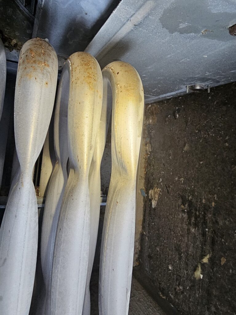 Close-up of furnace heat exchanger tubes with rust spots on the upper bends beside a dirty, dark cabinet wall