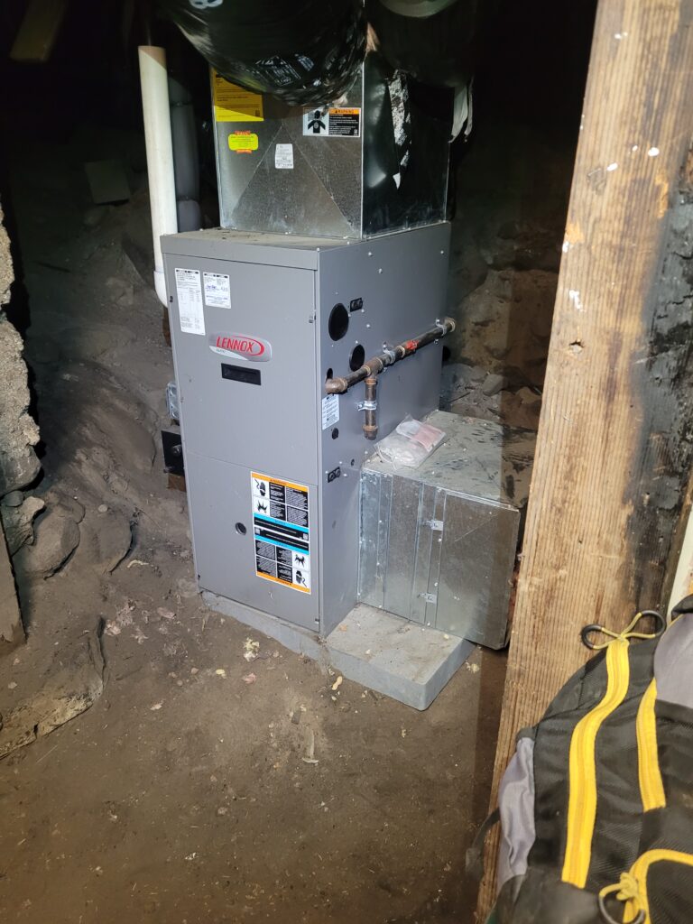 New gray Lennox gas furnace on a concrete pad in a dirt-floor crawlspace, with sheet metal plenum, side return and gas line