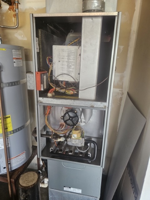 Gas furnace with front panels removed, showing control board, wiring, gas valve and burners beside a water heater