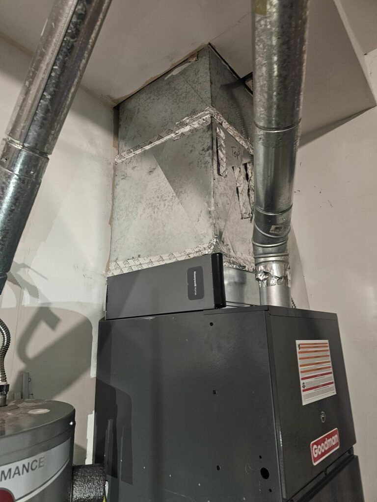 Gray Goodman furnace with Honeywell media air cleaner and sealed galvanized supply plenum, beside a water heater and metal vent pipes