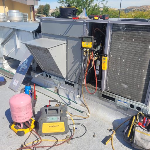HVAC technician servicing a commercial rooftop packaged unit with Fieldpiece recovery machine, R-410A refrigerant tank, and digital manifold gauges connected to the system