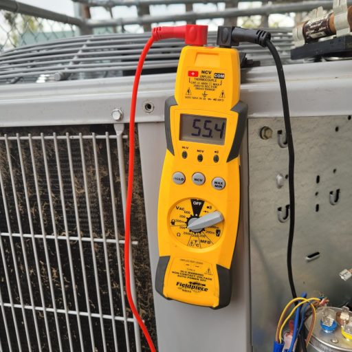 Fieldpiece HS33 multimeter displaying 55.4 MFD while testing a capacitor on an outdoor HVAC condenser unit