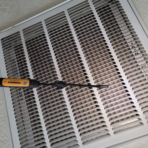 Fieldpiece temperature probe inserted into a ceiling HVAC return air vent with a dirty filter visible behind the grille