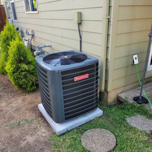 Goodman air conditioning condenser unit installed on a concrete pad beside a house with beige siding